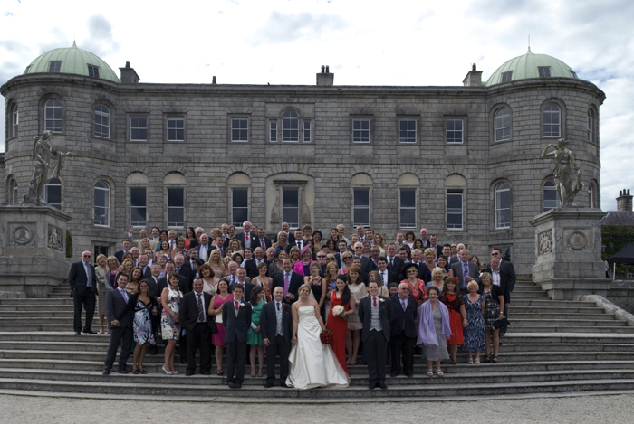 The bride and groom stand with their guests on the steps of Powerscourt Estate 