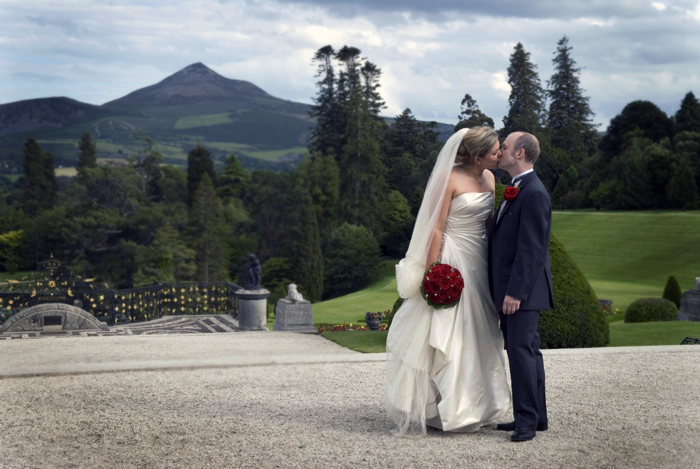 The bride and groom stand for a wedding photograph in the grounds of The Powerscourt Estate with the Sugarloaf Mountain in the background.
