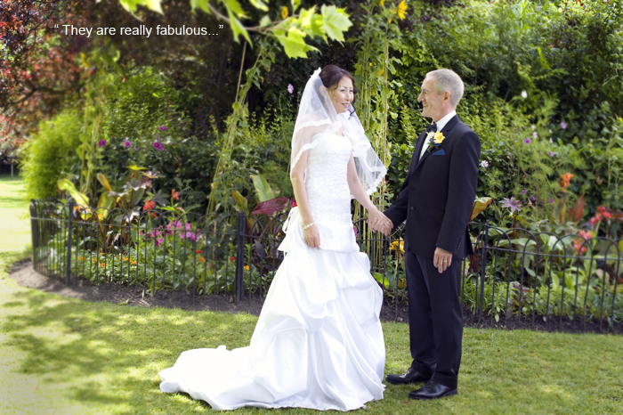 The bride and groom hold hands and pose for a wedding photograph by flowers in St. Stephen's Green in Dublin